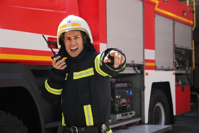 Photo of Firefighter in uniform using portable radio set near fire truck outdoors
