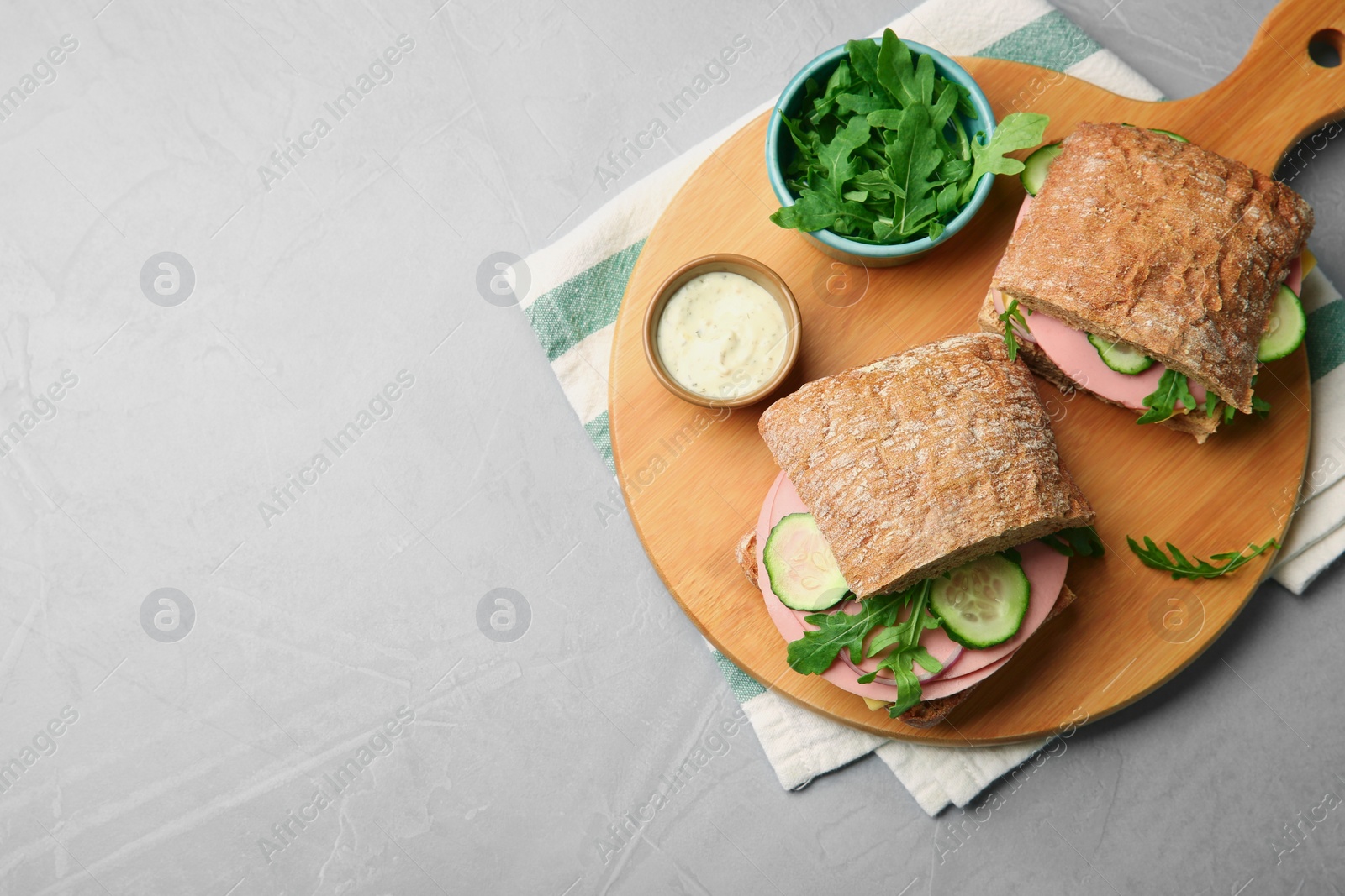 Photo of Tasty sandwiches with boiled sausage, cucumber, arugula and sauce on grey table, top view. Space for text