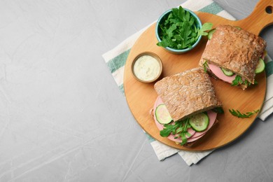 Tasty sandwiches with boiled sausage, cucumber, arugula and sauce on grey table, top view. Space for text