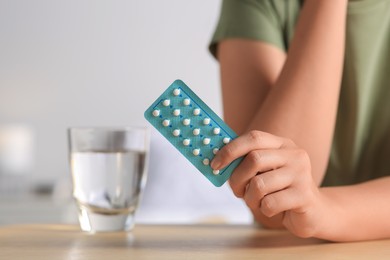 Photo of Woman taking oral contraception pill at wooden table indoors, focus on hand