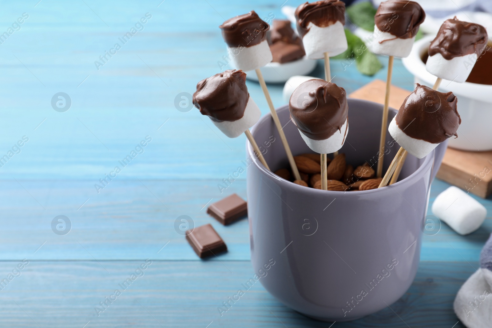 Photo of Delicious marshmallows covered with chocolate on blue wooden table. Space for text