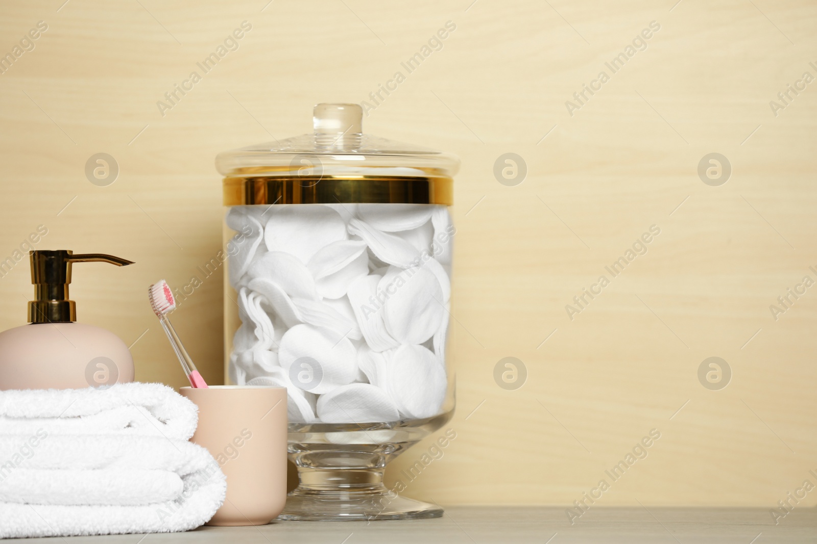 Photo of Composition of glass jar with cotton pads on table near light wooden wall. Space for text