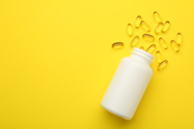 Softgel capsules and bottle on yellow background, top view. Space for text