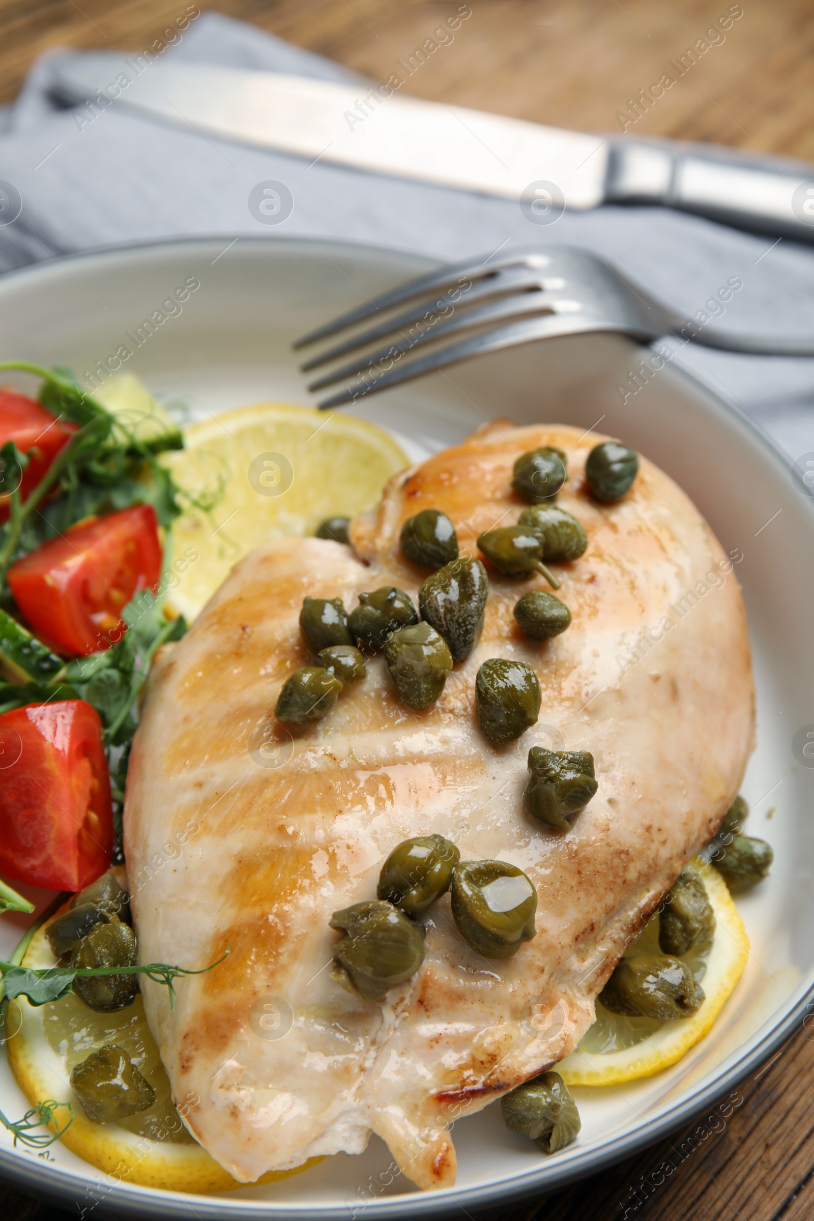 Photo of Delicious cooked chicken fillet with capers and salad served on table, closeup