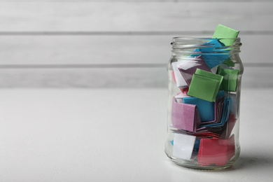 Glass jar with colorful paper pieces on white table, space for text