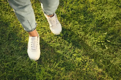 Photo of Woman in jeans and white shoes walking on green grass, closeup. Space for text