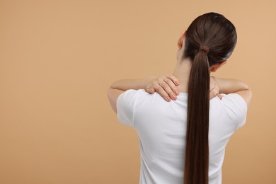 Woman touching her neck on beige background, back view. Space for text
