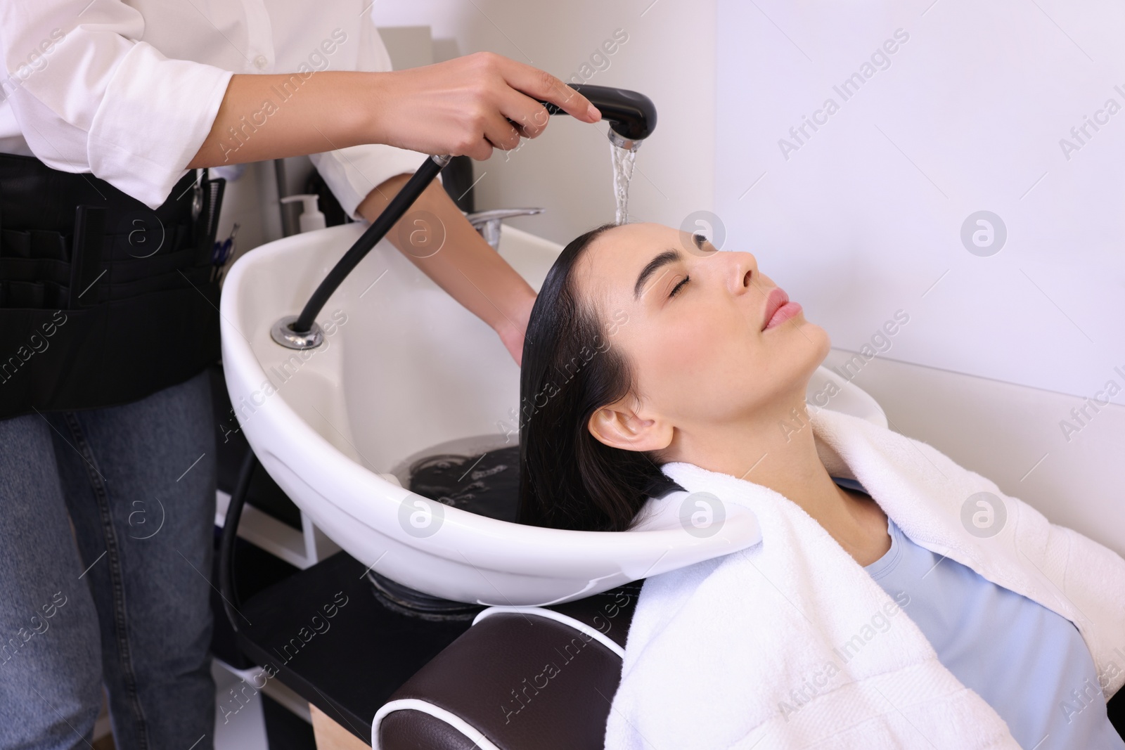 Photo of Professional hairdresser washing woman's hair in beauty salon, closeup