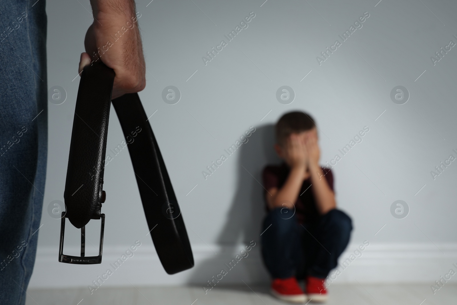 Photo of Man threatening his son with belt indoors, closeup. Domestic violence concept