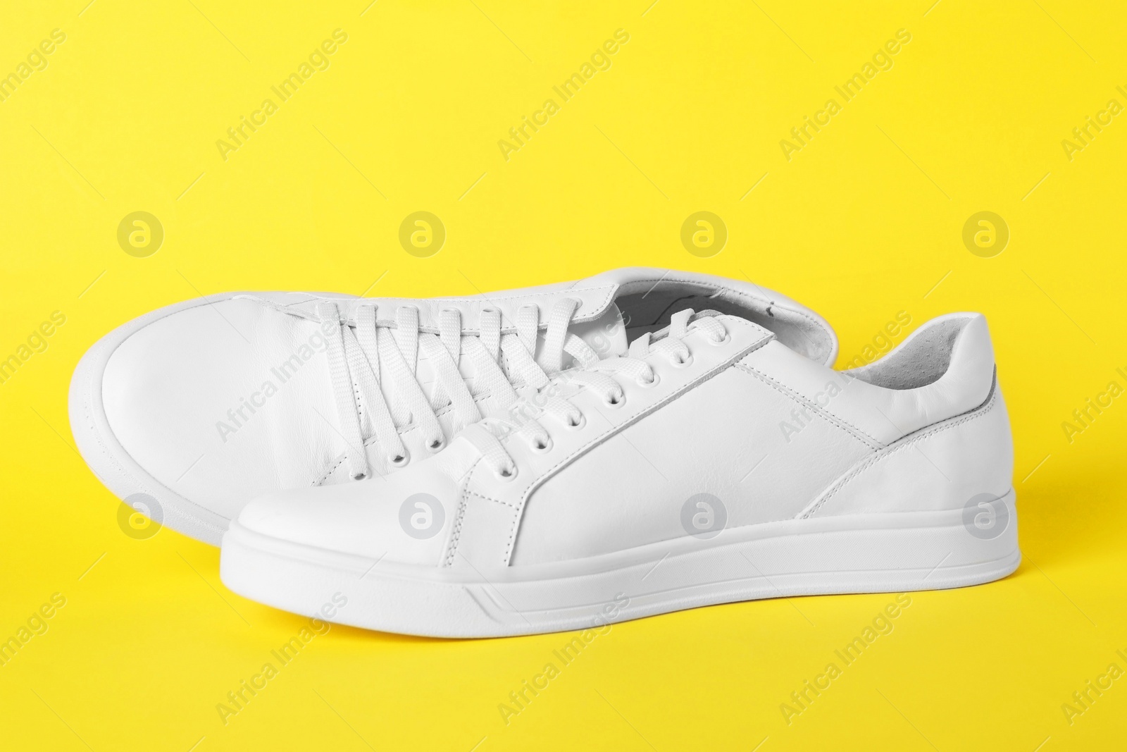 Photo of Pair of stylish white sneakers on yellow background