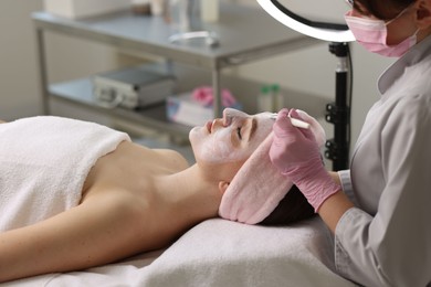 Photo of Cosmetologist applying mask on woman's face in clinic, closeup