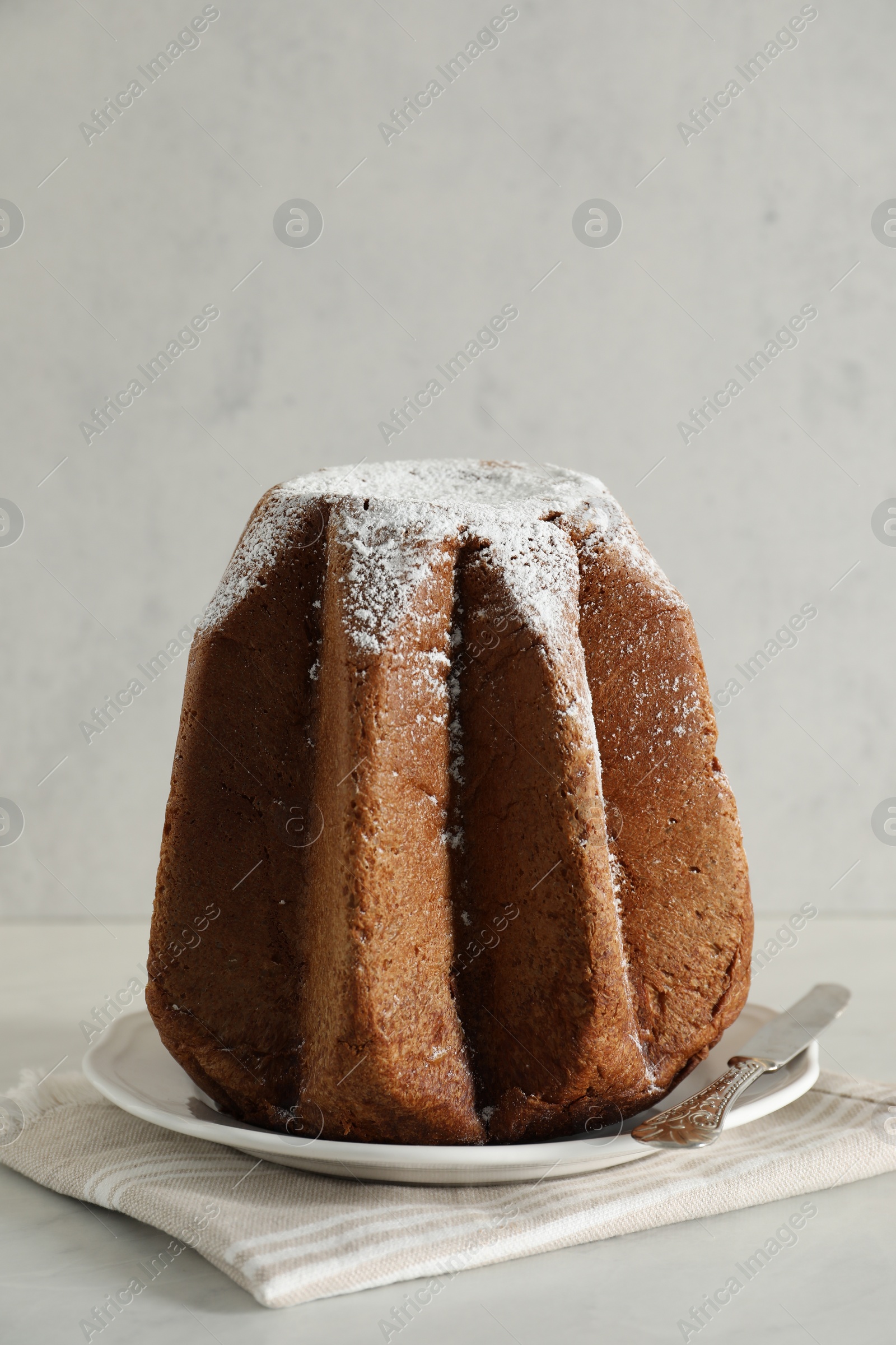 Photo of Delicious Pandoro cake decorated with powdered sugar on white table. Traditional Italian pastry