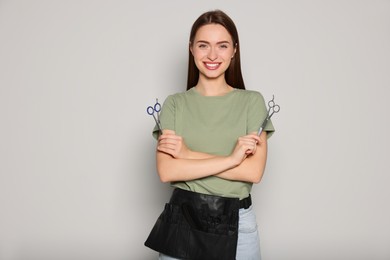 Portrait of happy hairdresser with professional scissors on light background. Space for text