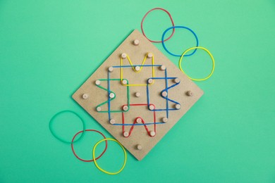 Wooden geoboard with rubber bands on green background, flat lay. Educational toy for motor skills development
