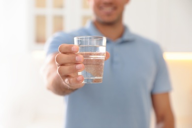 Man holding glass of pure water in kitchen, closeup