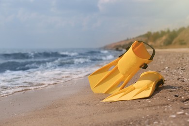 Pair of yellow flippers on sand near sea. Space for text