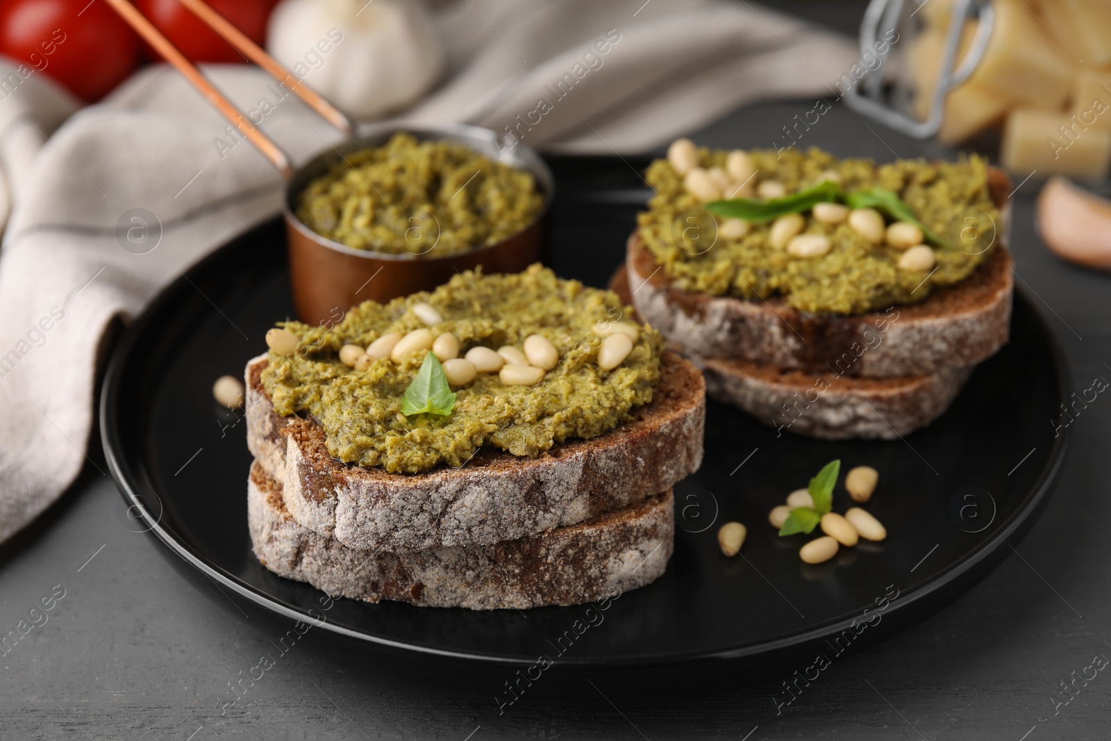 Photo of Tasty bruschettas with pesto sauce and nuts on dark grey table, closeup