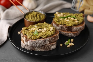 Photo of Tasty bruschettas with pesto sauce and nuts on dark grey table, closeup