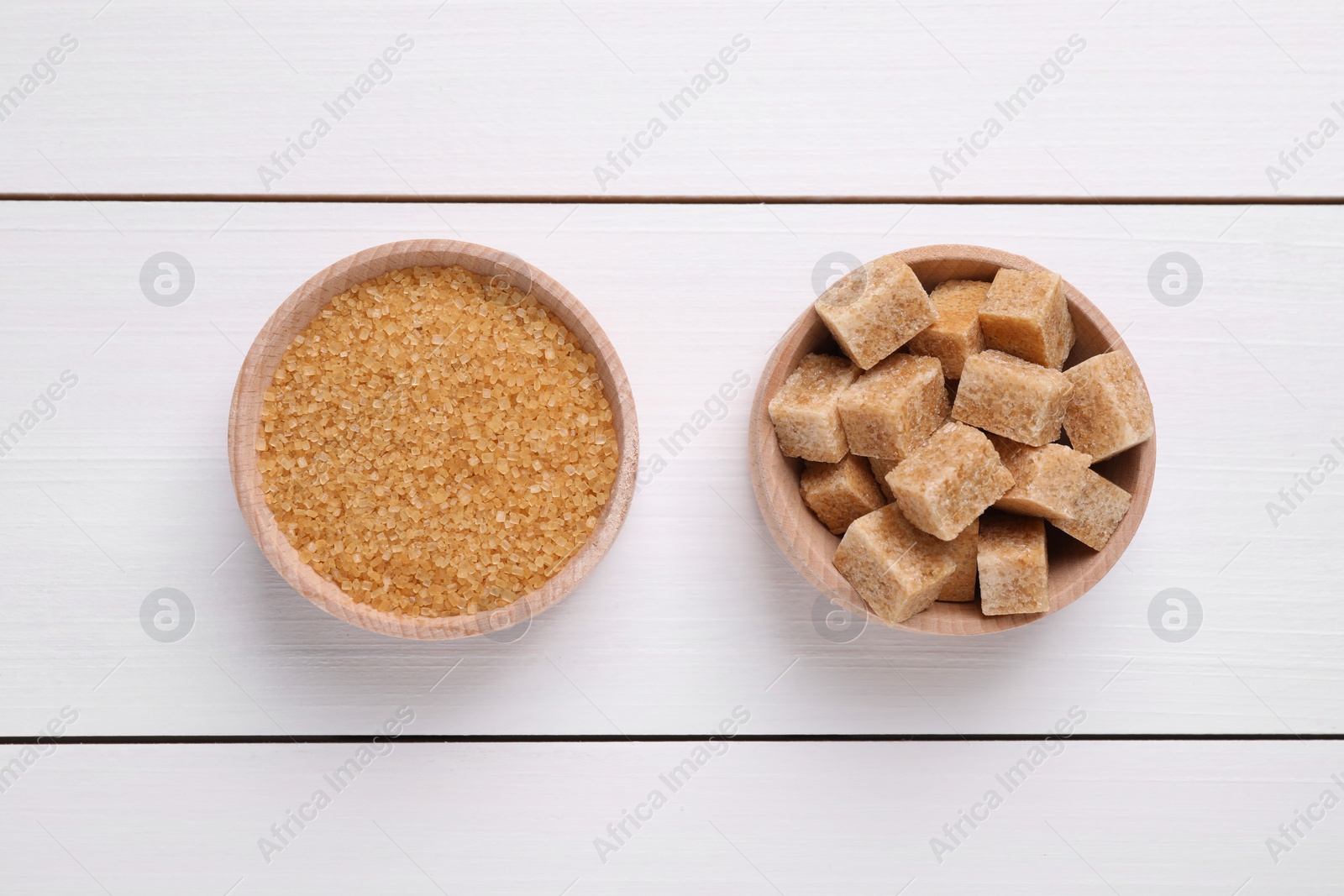 Photo of Different types of brown sugar in bowls on white wooden table, flat lay