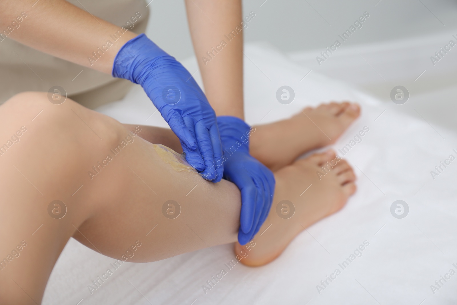 Photo of Woman getting wax epilation of legs in salon, closeup