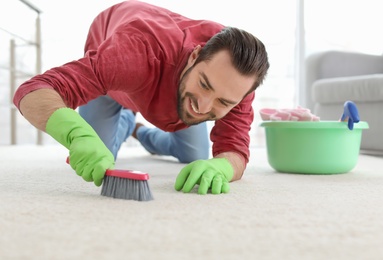 Photo of Young man cleaning carpet at home