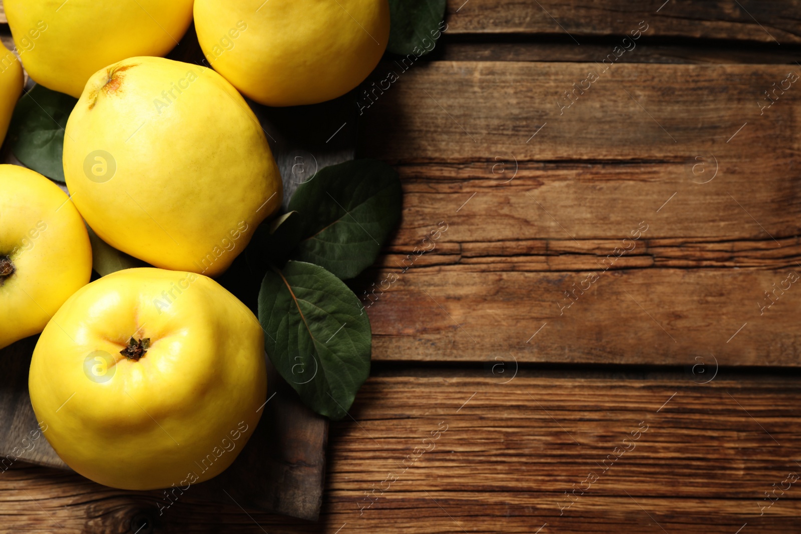 Photo of Fresh ripe organic quinces with leaves on wooden table, flat lay. Space for text