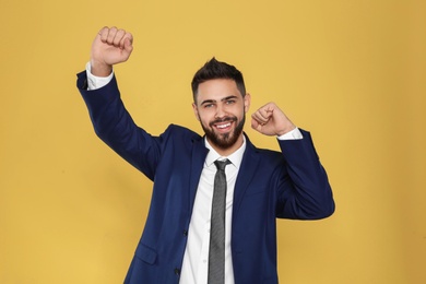 Happy young businessman celebrating victory on color background