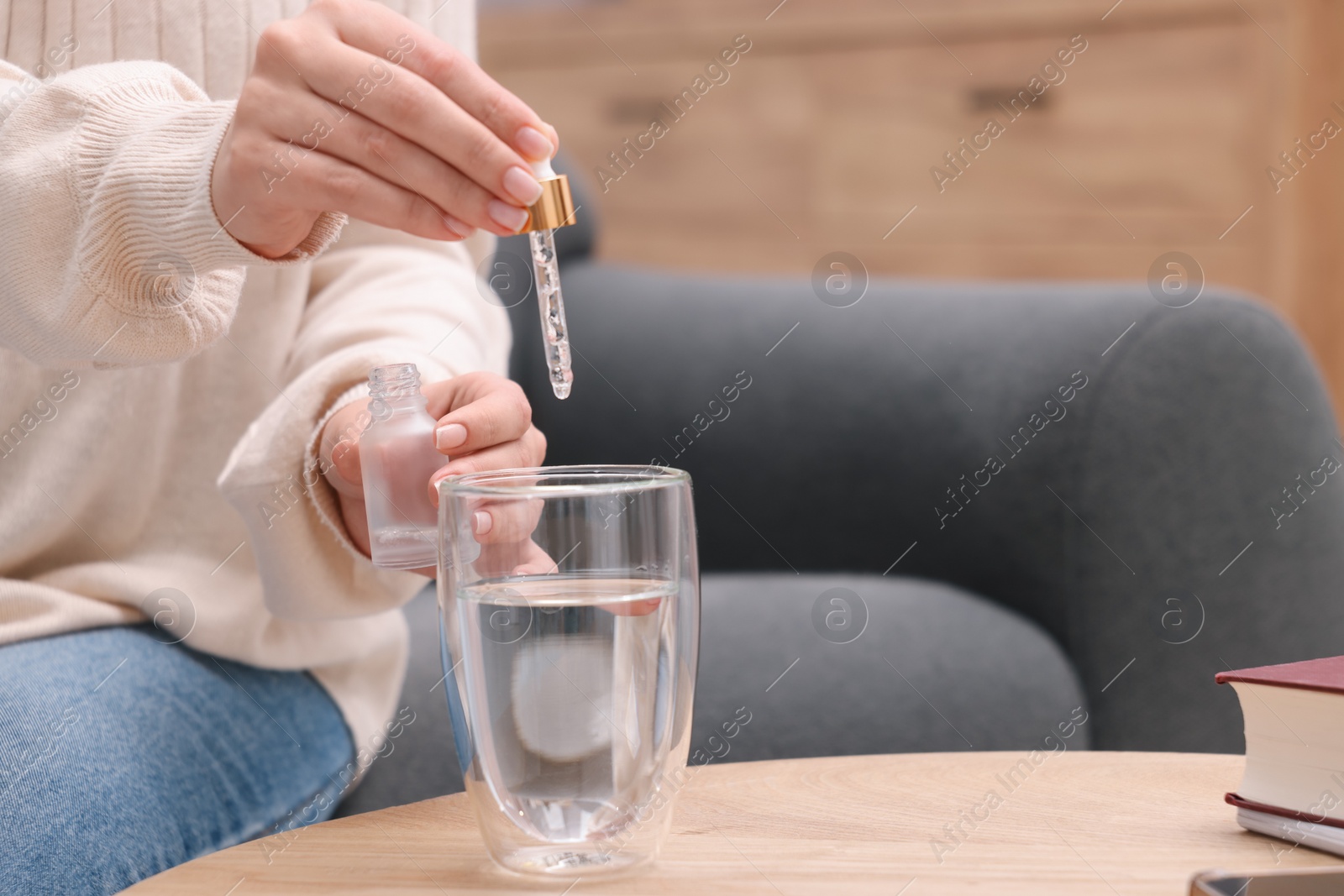 Photo of Woman dripping food supplement into glass of water on wooden table indoors, closeup. Space for text