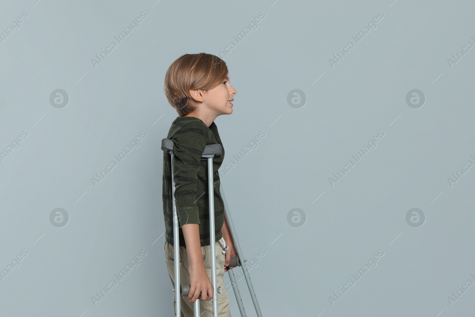 Photo of Portrait of happy boy with crutches on grey background. Space for text