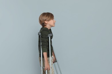 Photo of Portrait of happy boy with crutches on grey background. Space for text