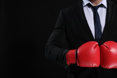 Photo of Businessman in suit wearing boxing gloves on black background, closeup. Space for text