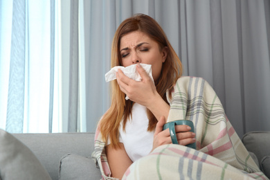 Photo of Sick woman wrapped in plaid with cup of hot drink at home. Influenza virus