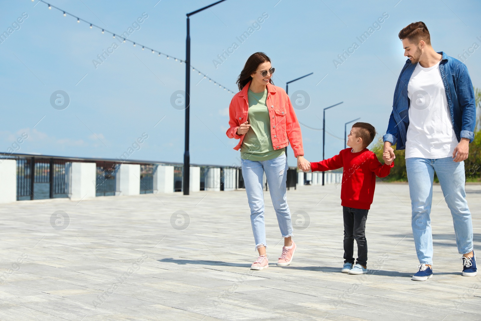 Photo of Happy child holding hands with his parents outdoors, space for text. Family weekend