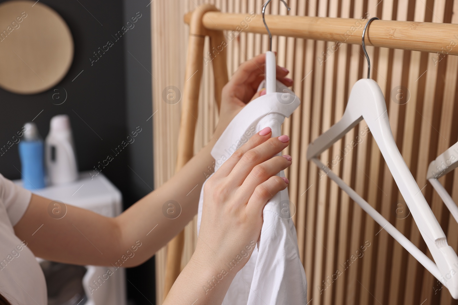 Photo of Woman taking shirt from rack in laundry room, closeup