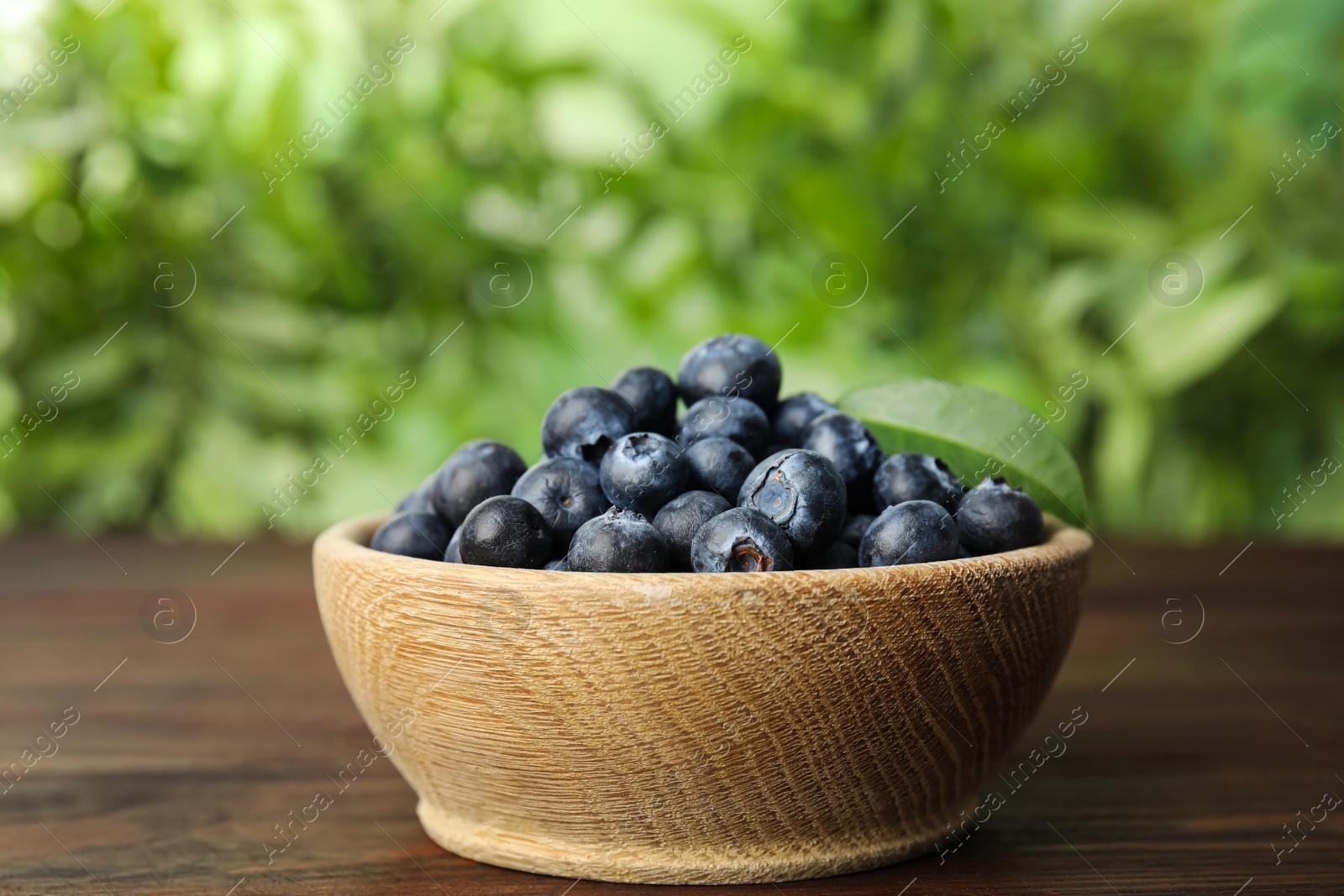 Photo of Tasty ripe blueberries in bowl on wooden table