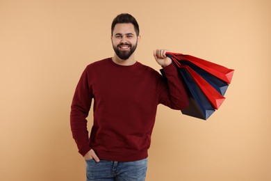 Smiling man with many paper shopping bags on beige background
