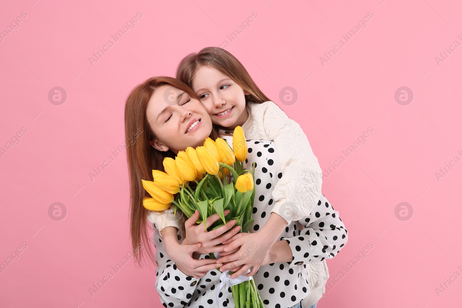 Photo of Mother and her cute daughter with bouquet of yellow tulips on pink background