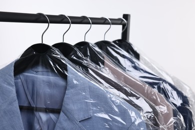 Dry-cleaning service. Many different clothes in plastic bags hanging on rack against white background, closeup