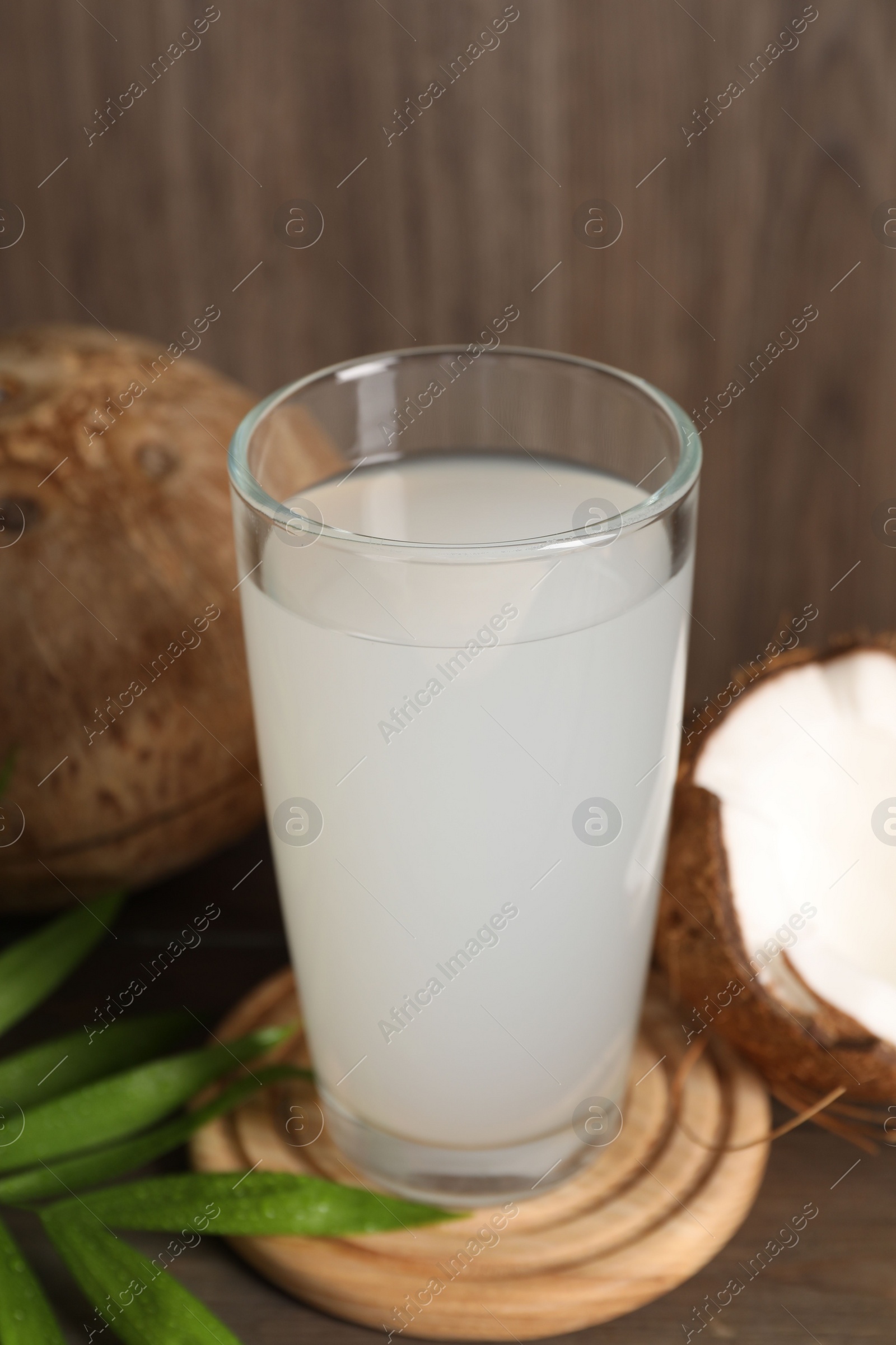 Photo of Glass of coconut water, leaf and nuts on wooden table