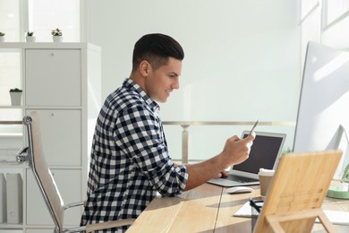 Photo of Freelancer using smartphone while working on laptop at table indoors