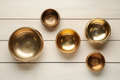 Photo of Golden singing bowls on white wooden table, flat lay