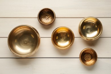 Golden singing bowls on white wooden table, flat lay