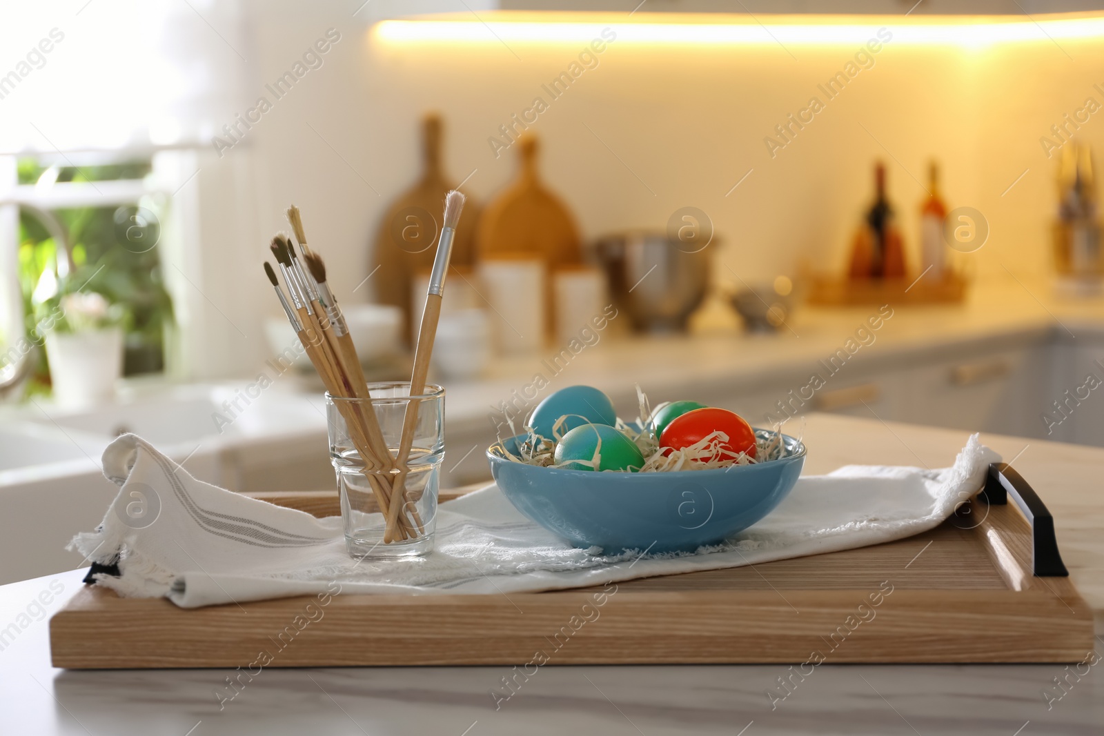 Photo of Beautifully painted Easter eggs in bowl and brushes on table indoors