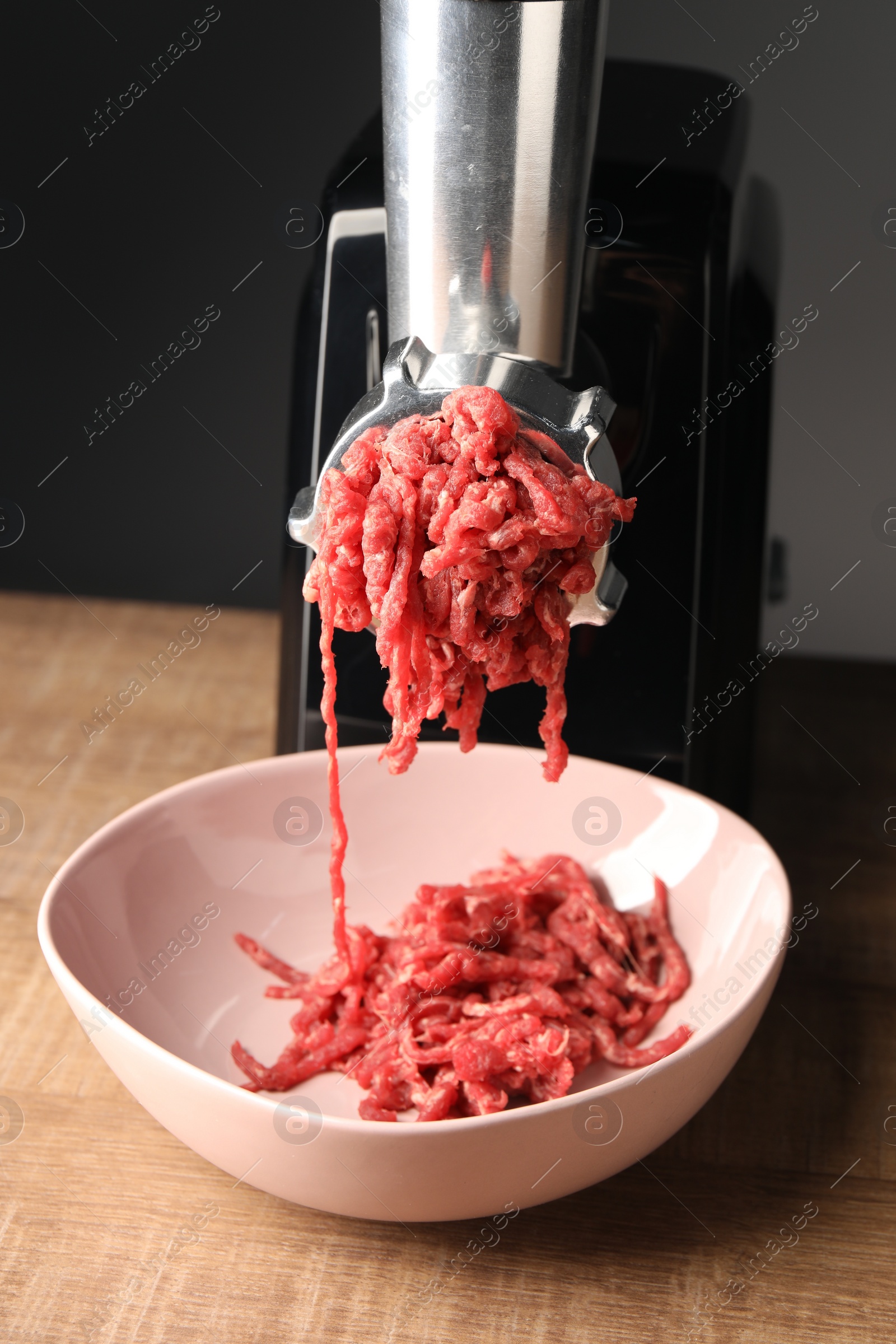 Photo of Electric meat grinder with beef mince on wooden table