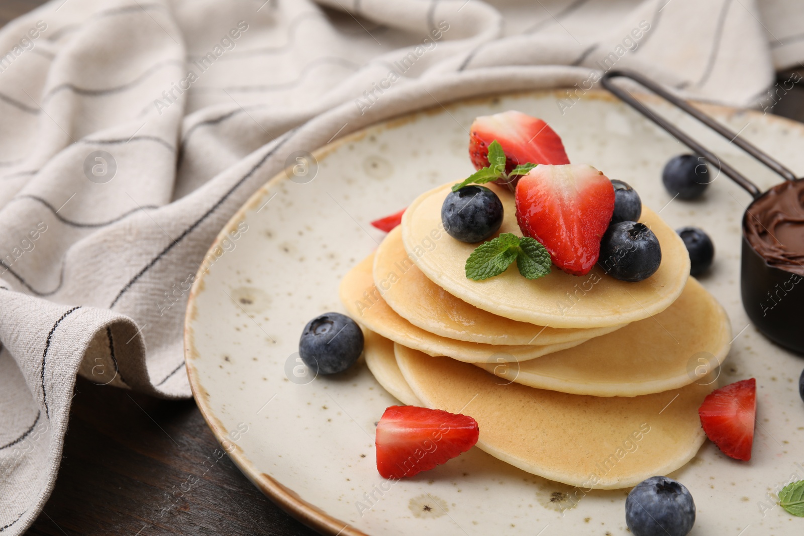 Photo of Delicious pancakes served with berries and chocolate spread on wooden table, closeup