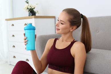 Photo of Woman with bottle of protein shake near sofa in living room