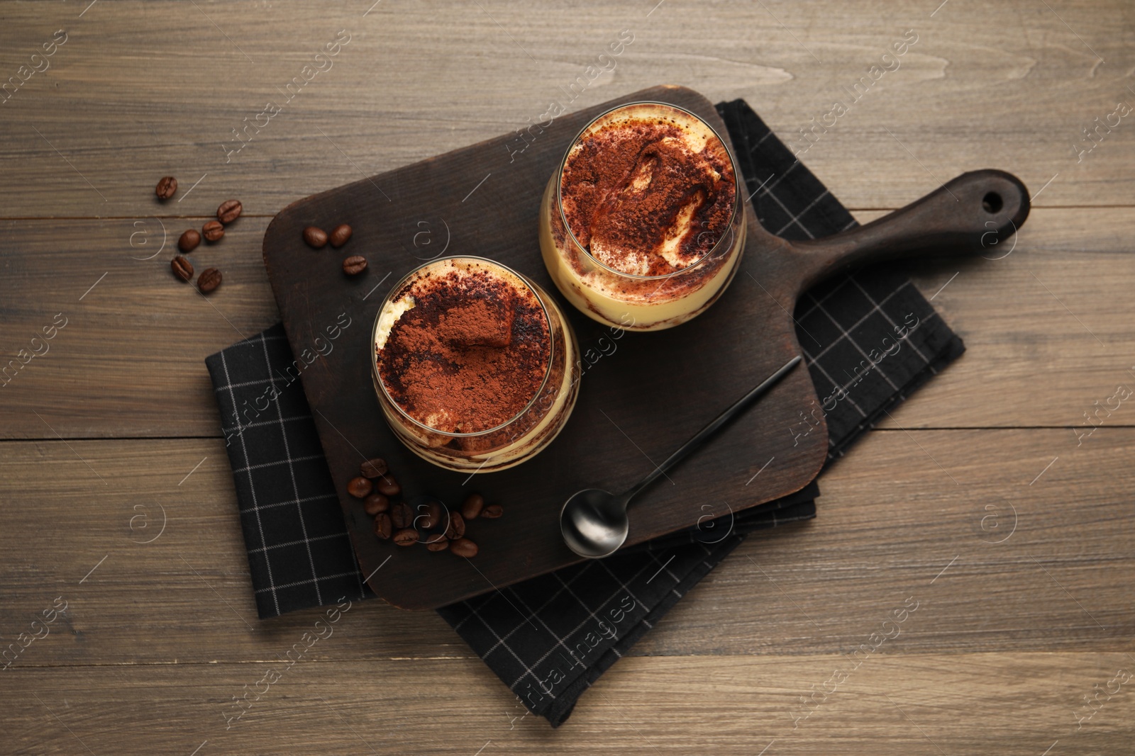 Photo of Delicious tiramisu in glasses, spoon and coffee beans on wooden table, top view