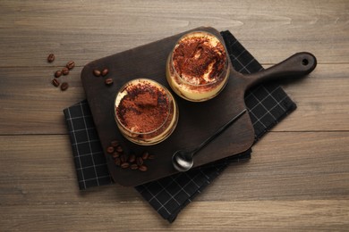 Delicious tiramisu in glasses, spoon and coffee beans on wooden table, top view