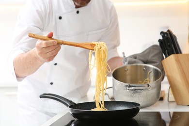 Photo of Chef putting delicious spaghetti from pot into frying pan indoors, closeup
