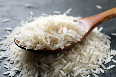 Photo of Raw basmati rice and wooden spoon on black table, closeup